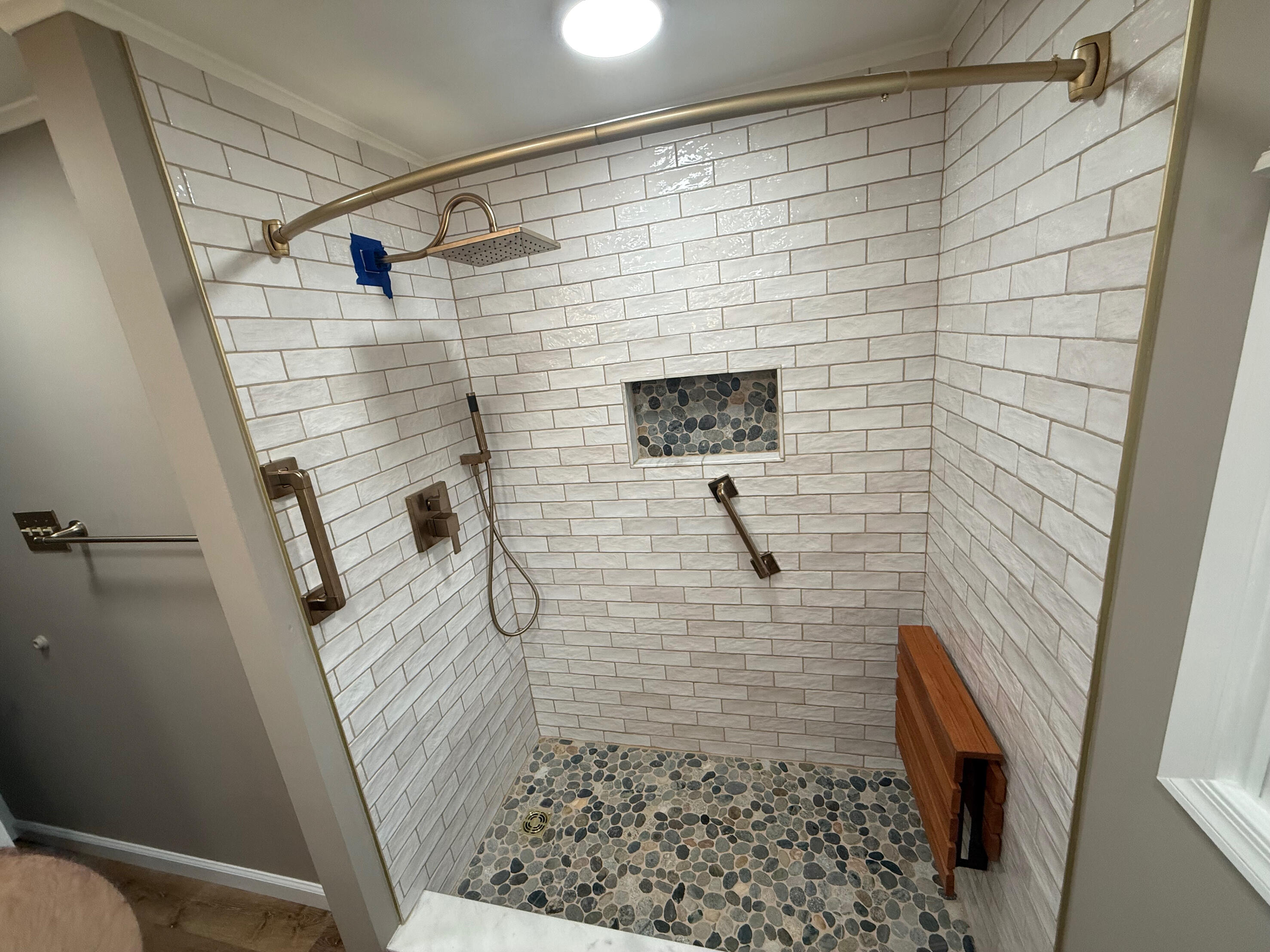 JLC Kitchen & Bath Remodeling White tiled walk-in shower with pebble floor, recessed niche and grab bars